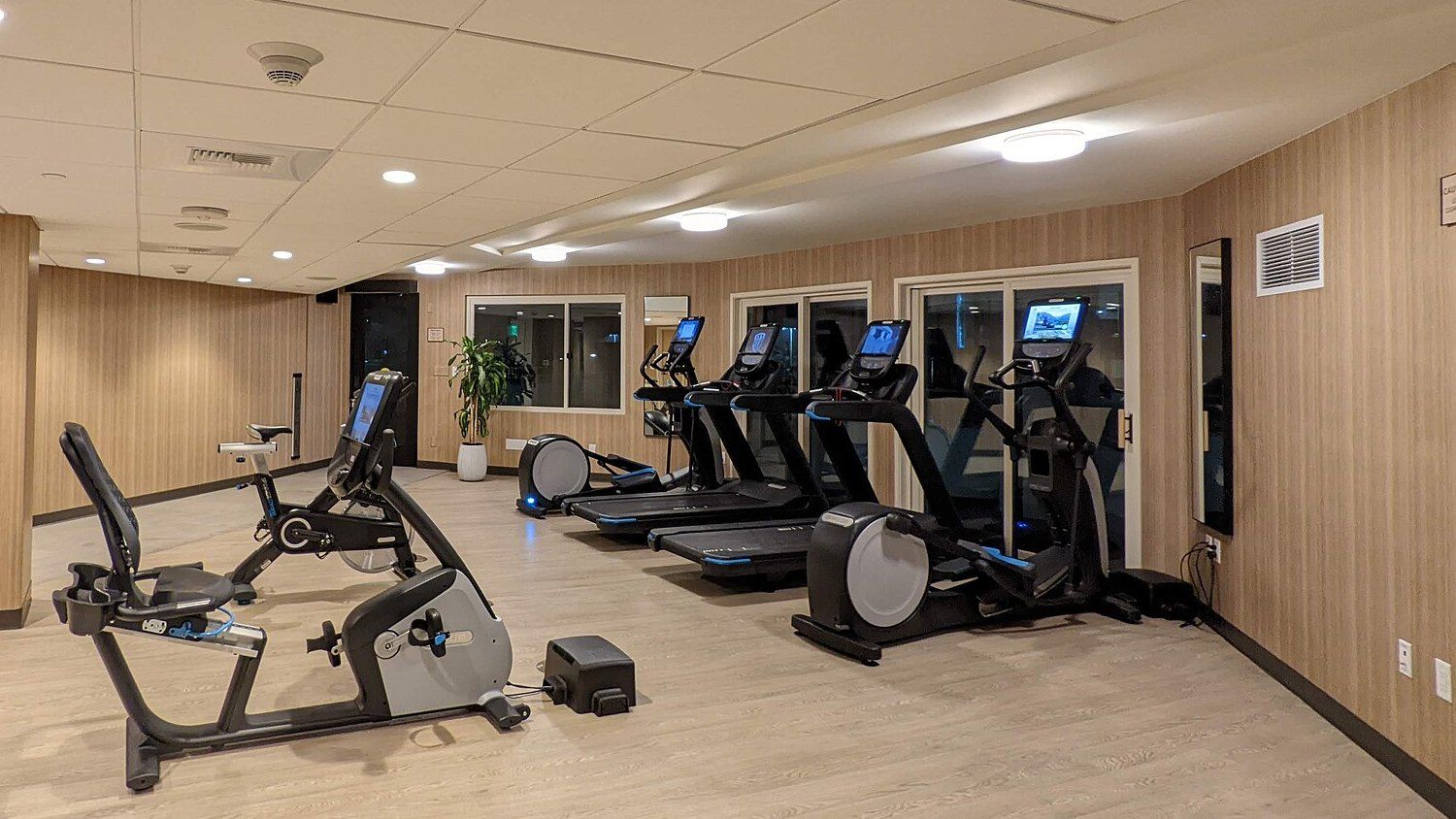 A hotel fitness room with a row of commercial treadmills between two elliptical trainers, with a recumbent bike and an upright bike in the foreground